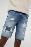 Bermuda azul medio en jean con diseños de rotos y parches