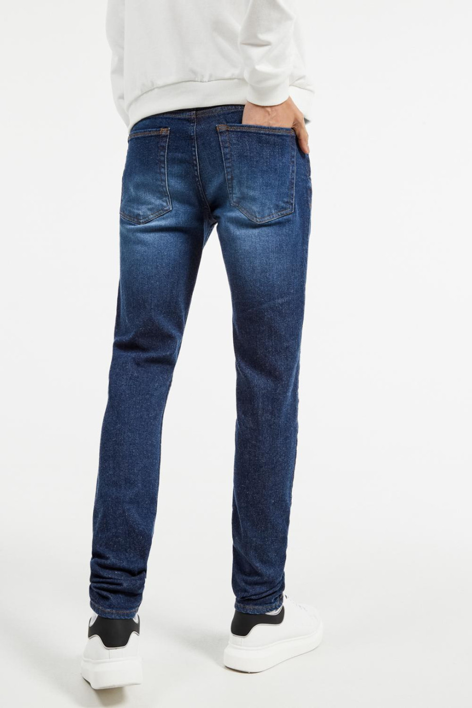 Jean azul oscuro tipo slim con 5 bolsillos, tiro bajo y costuras cafés
