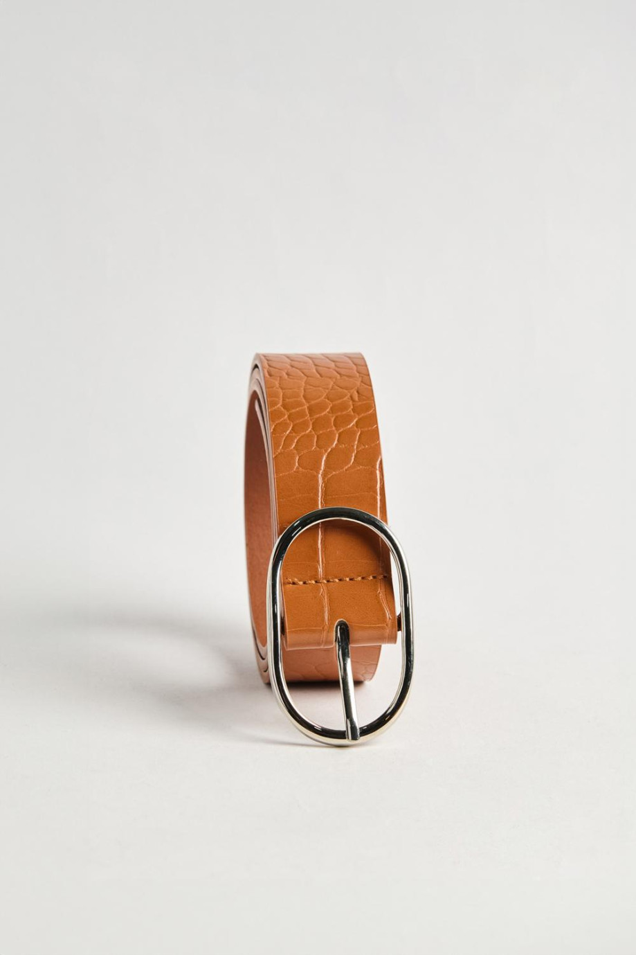 Cinturón femenino en color camel, elaborado en sintético con textura tipo reptil, hebilla metálica ovalada y punta con forma esp